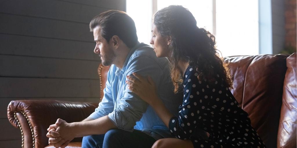 Woman comforting man on sofa